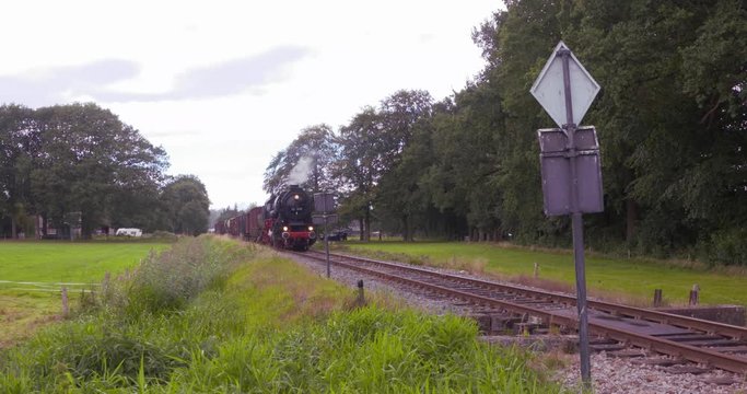 oncoming steam hauled freight train + whistle. Steam locomotive 44 1593-1 (1943, Lille) with vintage freight wagons. VELUWE, THE NETHERLANDS