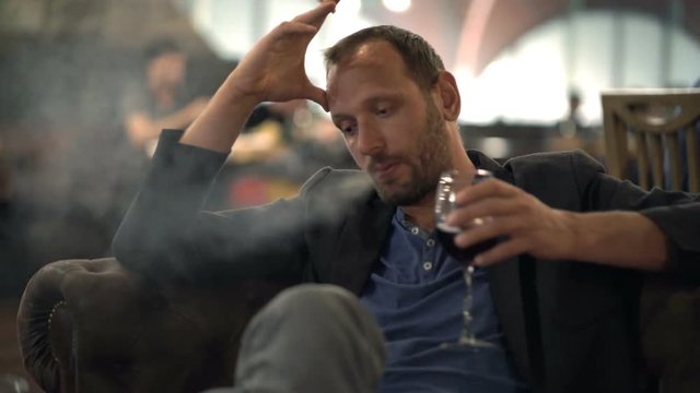 Sad man smoking cigarette and drinking wine in cafe
