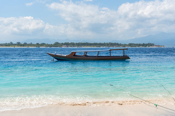 Fototapeta na wymiar Small wooden boat on blue beach with cloudy sky and Lombok island on background. Gili Trawangan, Indonesia.