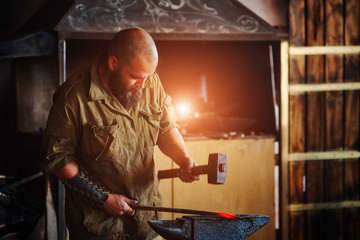 Blacksmith working in the forge. Manufacture of parts and weapons from molten metal, using the hammer and anvil.