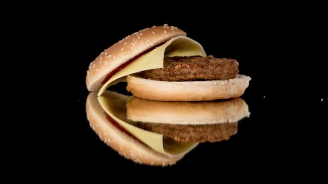 Hamburger covered with seeds and filled with beef burger and cheese faling down.