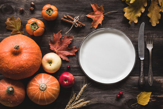 Autumnal table setting for Thanksgiving dinner. Empty plate, cutlery, pumpkins, apples and spices on wooden table. Fall food concept