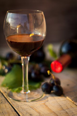 Wine glass with black wine. Bottle of wine and grapes in the background