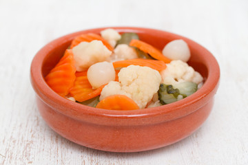 Pickled vegetables in ceramic dish on wooden background
