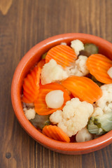 Pickled vegetables in ceramic dish on wooden background