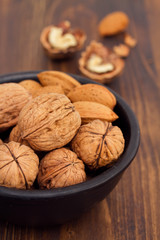 walnuts and almond on black bowl on brown wooden background