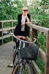 Obraz premium Yong stylish woman in black cardigan with pretty retro bicycle with busket in park.