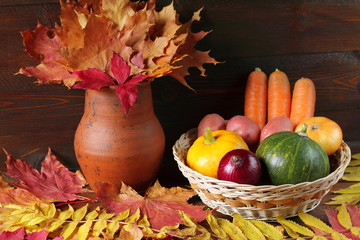 Autumn still life. A wicker basket with vegetables and autumn foliage on a dark wooden background.