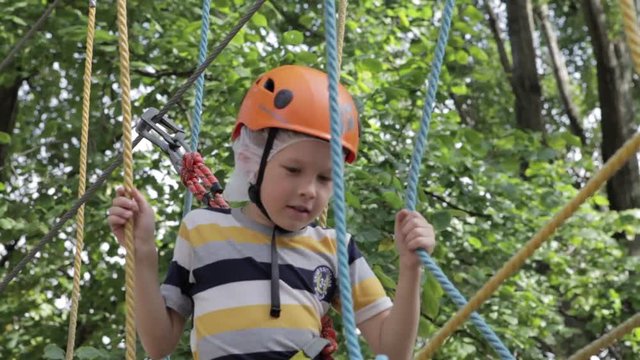 Little cute boy enjoying activity in a climbing adventure park on a summer sunny day. toddler climbing in a rope playground structure. Safe Climbing extreme sport with helmet and Carabiner. insurance