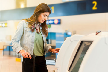 Young woman with trolley bag using self check-in machine in airport. 