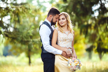 Stylish couple of happy newlyweds posing in the park on their wedding day. Perfect couple bride, groom posing and kissing 
