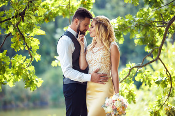 Stylish couple of happy newlyweds posing in the park on their wedding day. Perfect couple bride, groom posing and kissing 
