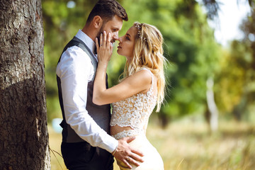 Fototapeta premium Stylish couple of happy newlyweds posing in the park on their wedding day. Perfect couple bride, groom posing and kissing 