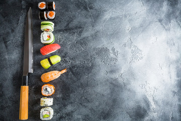 Traditional Japanese food - sushi, rolls, rice with shrimp and knife on a dark background. Top view