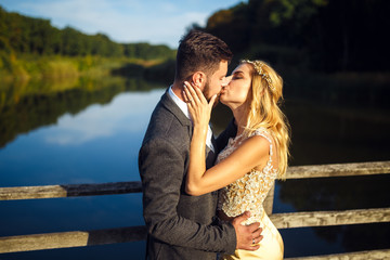 Stylish couple of happy newlyweds posing in the park on their wedding day. Perfect couple bride, groom posing and kissing 
