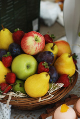 Wicker straw basket with an assortment of fruits, grape, strawberry, apples, pears, on a wooden table in a rustic style, top view