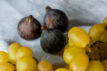 three black figs with bunch of white grapes on a white cloth