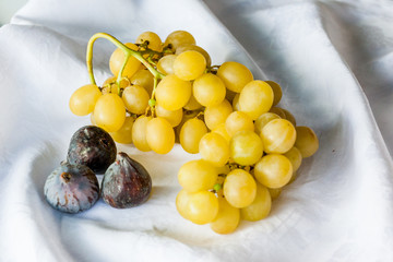 three black figs with bunch of white grapes on a white cloth