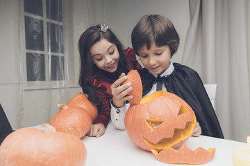 A boy in a black cloak made a beautiful, scary pumpkin for Halloween, a girl in a red dress is ecstatic