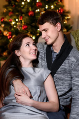 Fototapeta premium A beautiful couple hugging and looking happily at each other, christmas eve together. Couple cuddling and laughing on sofa.