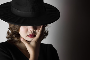 Beautiful young woman wearing black dress, black hat and red lips in the dark concept, Concept : dark, halloween, mysterious, depressed