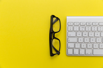 Computer keyboard + reading glasses on bright yellow background