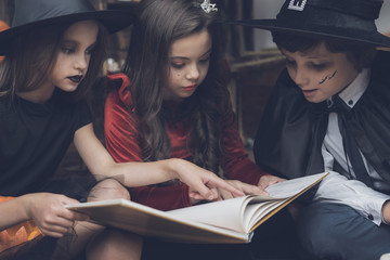 Three children sit on the floor and read the old book of spells for Halloween