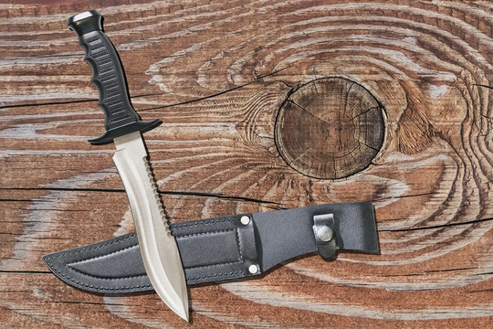 Combat Hunting Survival Sawback Bowie Knife With Black Leather Sheath Set On Old Cracked Knotted Rustic Pinewood Background