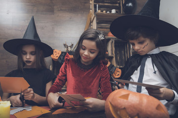 Three children in costume fairy monsters at the Halloween party cut out bats from paper