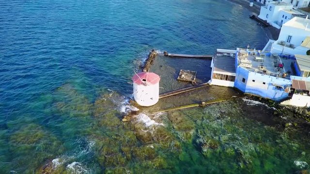 August 2017: Aerial drone video of iconic windmill built in a rock next to the coast with clear turquoise waters, Leros island, Aegean, Dodecanese, Greece