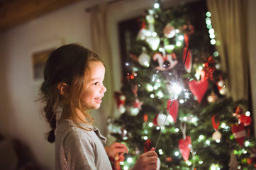 Little girl with a sparkler in front of Christmas tree.