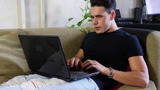 Preoccupied, worried young male worker staring at laptop computer screen at home with alarmed expression, typing frantically