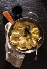 cooked ravioli in serving pan with parmesan and fried sage . on black stone background with glass of red wine