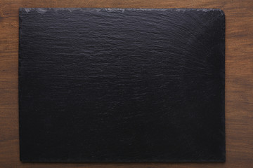 Empty rustic black slate stone plate on wooden background