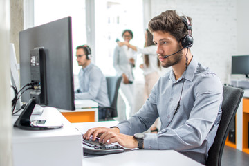 Young handsome male customer support phone operator with headset working in call center. - obrazy, fototapety, plakaty