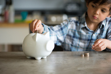 Boy insert a coin into his piggy bank