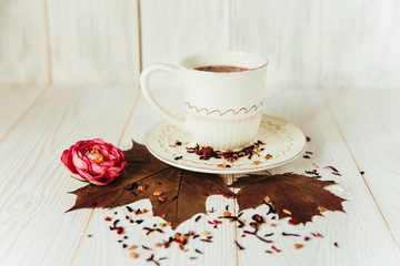 Cup with autumn elements on the white wood.Flower and leaves.Autumn composition.