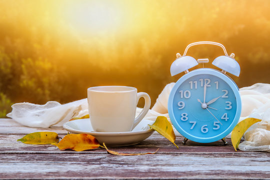 Image of autumn Time Change. Fall back concept. Dry leaves and vintage alarm Clock on wooden table outdoors at afternoon