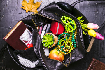 The contents of the female handbag. Flowers, lipstick, camera, coffee, biscuits, beads. Dark background.