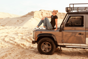 Fototapeta na wymiar Woman dreams of sitting on the hood of a car in the desert sands, she travels on off-road.