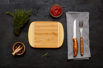 Empty cutting board pepper fork and knife on dark surface copy space background. Top view, flat lay.