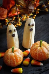 Halloween food Banana ghosts and Clementine Pumpkins on dark spooky background