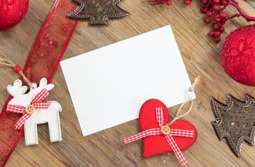 Christmas background with objects for decoration in Christmas tree, white sheet of blank paper and red festive ribbon on wooden table top. Space for text.