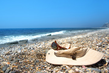 Old hat and sunglasses on the pebble beach of the Mediterranean Sea