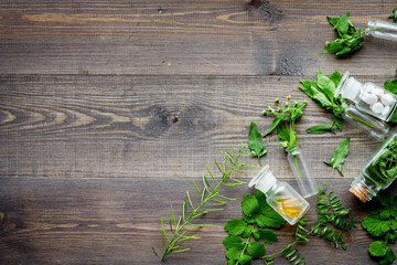 Homeopathy. Leaves of healing herbs, bottles and pills on wooden background top view copyspace