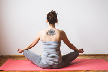 Back view of a tattooed woman meditating in the lotus position