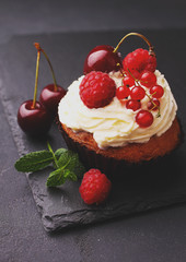 homemade cupcake with a cream, decorated with mint and berries on a black background.