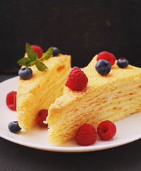 Napoleon cake decorated with raspberries, blueberries and mint on a white plate on a black background