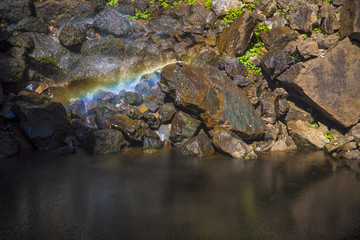 Magical Rainbow created by waterfall fallin on stone formation situated next to a water hole.