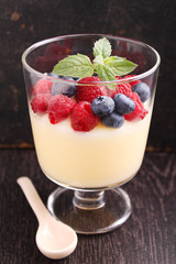 Milk pudding with berries in a glass on a black background